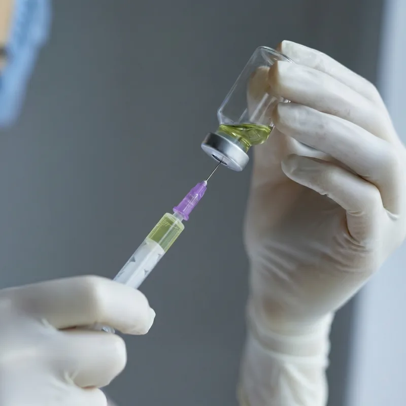 Gloved hands drawing a vial into a syringe